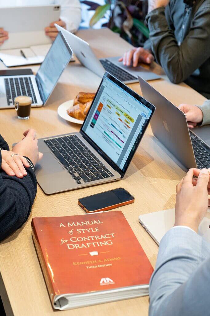 Equipe Klarc en reunion de travail autour d une table avec ordinateurs et un manuel de redaction de contrats